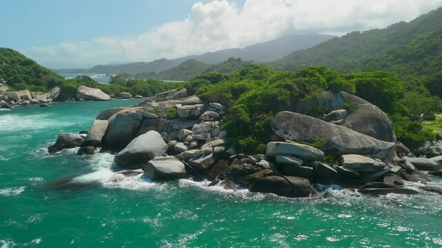 Aerial orbit of weathered granite boulders along rocky coast with turquoise water and jungle hills at Cabo San Juan in Parque Tayrona near Santa Marta Colombia
