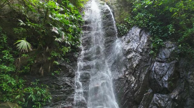 Tilt up from plunge pool to tall Teyumakke waterfall cascading down rock cliff through lush tropical jungle in Parque Tayrona near Santa Marta Colombia