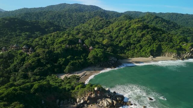 Aerial pullback rise revealing coastline of Playa Ca&ntilde;averal where jungle mountains meet turquoise Caribbean Sea in Parque Tayrona near Santa Marta Colombia