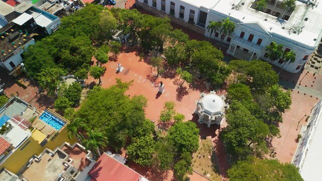 Aerial descent towards Parque de Los Novios with white gazebo Manuel Murillo Toro monument and red brick plaza framed by green trees in historic Santa Marta Colombia