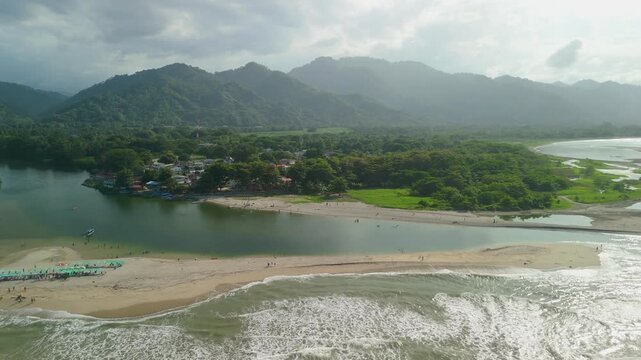 Aerial high altitude parallax over Buritaca village and sandbar where freshwater river meets Caribbean Sea below misty Sierra Nevada mountains near Santa Marta Colombia