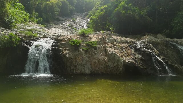 Low angle parallax of Quebrada Valencia waterfall cascading down rock face into emerald natural pool surrounded by lush jungle near Santa Marta Colombia