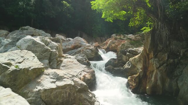 Aerial close-up flyover of Poza Encantada river rapids and whitewater chute rushing between smooth marble boulders through lush green jungle near Santa Marta Colombia