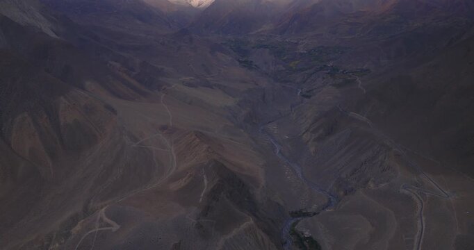 Drone glides to reveal direct sunlight striking mountain peaks in Mustang, Nepal, before sunset from the rocky terrain of the river valley and arid mountains