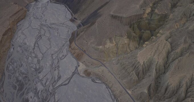 Aerial gliding shot in Mustang, Nepal, over a wide braided river network running alongside dry, rugged mountain canyon walls. and deserted landscape