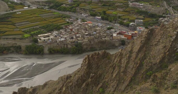 Kagbeni Mustang Nepal, aerial glide down along the hill shot to the historic mountain village nestled beside agricultural terraces, houses and a riverbed.