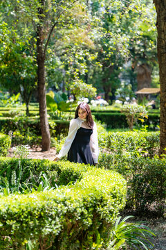 Young smiling latina woman posing relaxed, cheerful outdoors at Parque Mexico in Condesa, Ciudad de Mexico enjoying a sunny day surrounded trees and soft light, wearing a black dress with white blouse