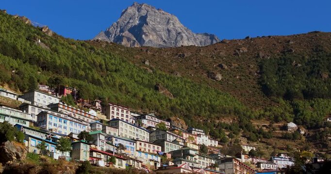 Namche Bazaar, Nepal. Sideways tracking drone shot showing hillside lodges below the rocky peak of Mount Khumbila under a clear blue sky