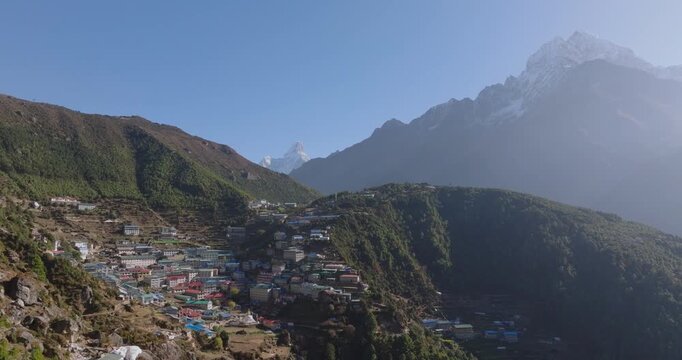 Namche Bazaar, Nepal, Slow push-in drone shot over the terraced mountain town, revealing Ama Dablam in the distance and Kongde Ri on the right under a blue sky