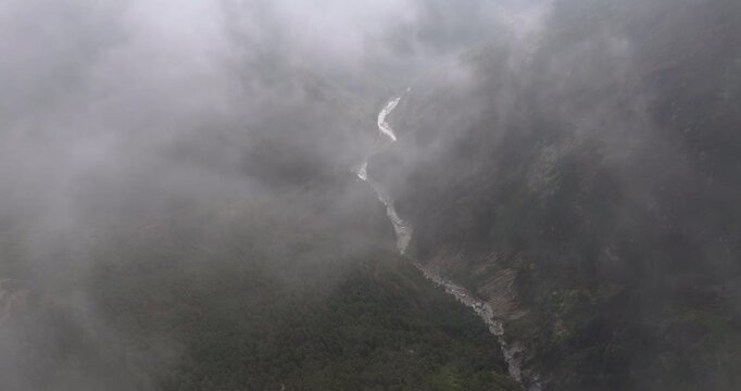 Khumbu region Nepal, a high angle aerial shot over a deep mountain gorge as swift, misty clouds rush past the camera, revealing the winding Bhote Koshi river valley below