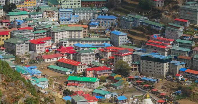 Namche Bazaar, Everest Region, Nepal, aerial lateral panning shot of village houses and modern lodges with colorful rooftops built on terraced land on a bright day.