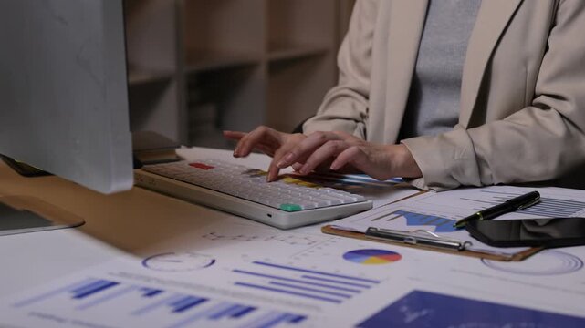 Businesswoman typing on computer keyboard working late night. Female accountant using a computer at her desk. Professional financial advisor analyzing company business data and reports at night.