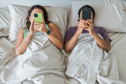 Couple ignoring each other using smartphones in bed