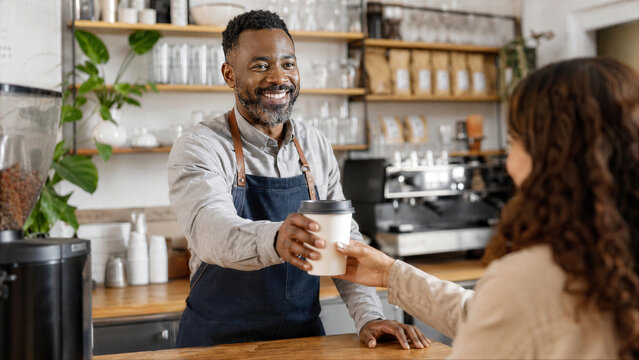 Black barista handing takeaway coffee in neighborhood cafe
