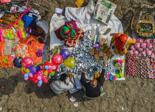 Bogura, Bangladesh - 12 February 2025: Aerial view of a vibrant local market featuring vendors selling colorful balloons, metal kitchenware, and various household items on the ground.