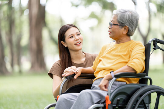 Asian Woman Holding Hands and Talking with Senior Mother in Wheelchair