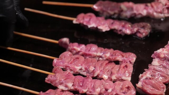 Close-up of raw chicken heart skewers (Tori Hatsu) being prepared on a grill for traditional Japanese Yakitori. This rare offal cut is a popular izakaya delicacy, known for its springy texture and ric