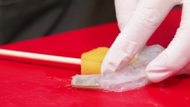 High-angle close-up of fresh, raw, butterflied prawns prepared on a vibrant red cutting board. The translucent white meat of the shrimp is displayed alongside a piece of yellow citrus, ready for gourm