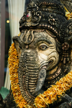 Close-up shot of Lord Ganesha sitting in meditating yoga pose at Villa entrance. Decorated for religious festival by orange flowers. Luck and Success's charm. Travel, Culture, Religion concept