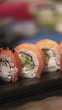 Vertical video. Sushi preparing. Garnishing food. Gloved chef hand adding black caviar on philadelphia rolls row salmon portion on plate.