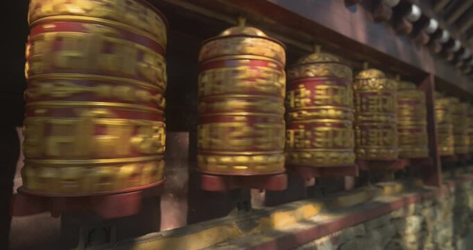 Namche Bazaar, Nepal, static shot of a person's hand spinning golden Buddhist prayer wheels engraved with sacred mantras outside a monastery.