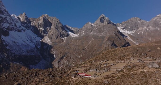 Everest region Nepal, drone orbit shot of traditional teahouses and stone wall settlements in Dole village beneath rugged alpine mountain landscapes.