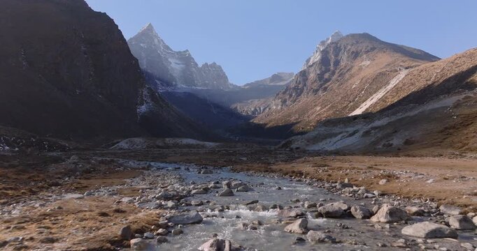 Everest region Nepal, aerial pull out shot of a flowing freshwater stream with a rocky bottom winding through an alpine valley beneath Mount Cholatse and Taboche peaks.