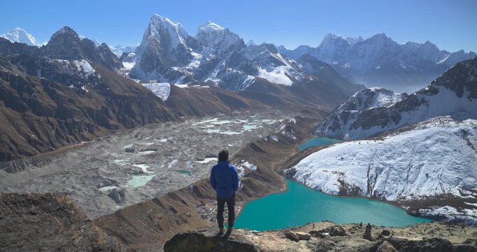 View from Gokyo Ri Everest region Nepal, a static camera shot as a trekker walks into the frame to look out over the Ngozumpa Glacier, turquoise Gokyo Lakes, and snow-capped Himalayan peaks.