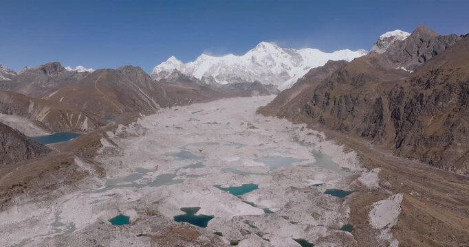 Ngozumpa Glacier, Everest Nepal, drone aerial pull out shot revealing the rugged glacial moraine and supraglacial meltwater pools beneath the massive snow capped peak of Cho Oyu