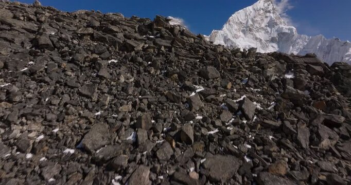 Kala Patthar Everest BaseCamp Nepal, drone sweeping past a dark rocky ridge to reveal the massive snow-capped summits of Mount Everest and Nuptse towering against a deep blue sky