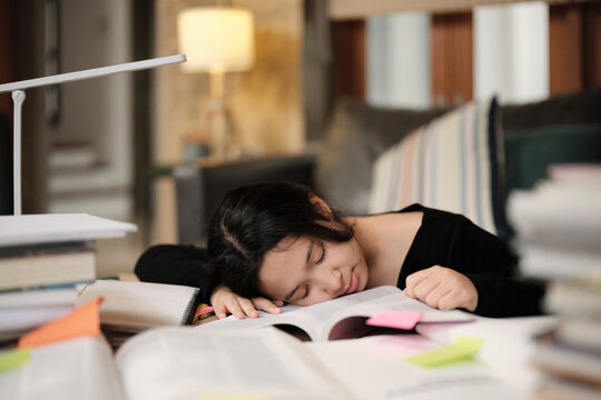 College Asian teenage girl tired and burned out from overwhelmed study pile of books, stressed learning at home with pile of textbooks, reading and writing for school exam, homeschooling education.