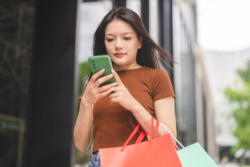 Online shopping, Smiling asian woman holding shopping bags using smartphone, digital payment...