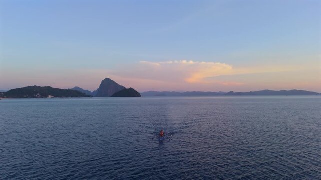 Lone paddler moves across open water toward distant limestone islands beneath pastel evening clouds