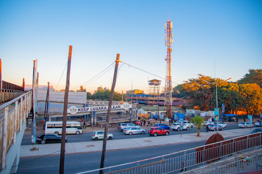 Lusaka, Zambia - 12 June 2026: View of a busy street scene with cars, a pedestrian bridge featuring a 'Keep Lusaka Clean' sign, and a tall telecommunications tower under a clear sky.