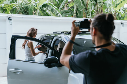 Photographer shooting female model posing with white car
