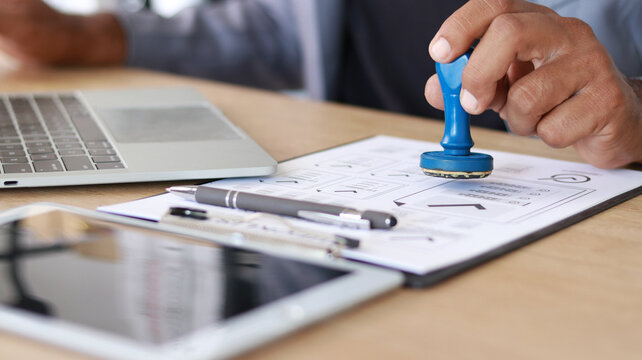 Business professional stamping approved documents on office desk with laptop and paperwork. Compliance, authorization, certification, verification, business process and corporate approval concept.