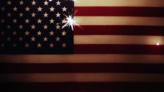 Sparks flying off a burning sparkler with sparks lighting up the dark shadows of an old USA flag. For patriotic 4th of July, US Memorial Day, Veteran's Day, or other patriotic American holiday. Loop.