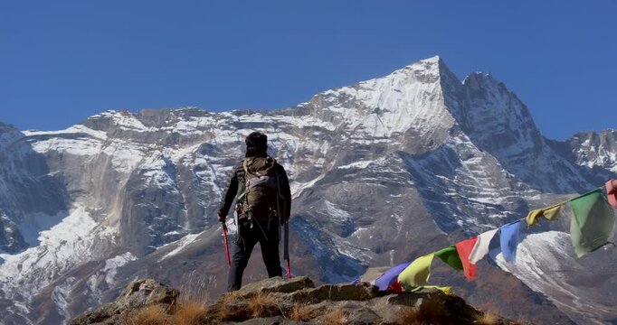 Everest Region, Nepal circular drone shot of a man standing atop a high-altitude mountain cliff, surrounded by a bright panoramic view of theMount Everest and other mountains