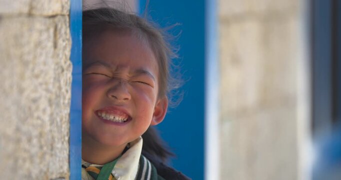 Namche, Everest, Nepal, close-up static shot of a young local schoolgirl squinting and smiling brightly before stepping back inside a classroom at a remote village school.