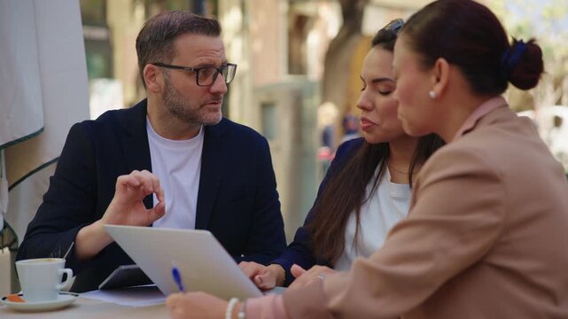 Diverse multi-ethnic business team having a collaborative meeting with a laptop and digital tablet at an outdoor cafe.