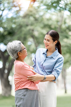 Happy Asian adult daughter embracing her smiling senior mother in the park