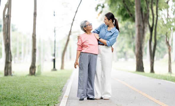 Happy adult daughter embracing her senior mother while walking in the park