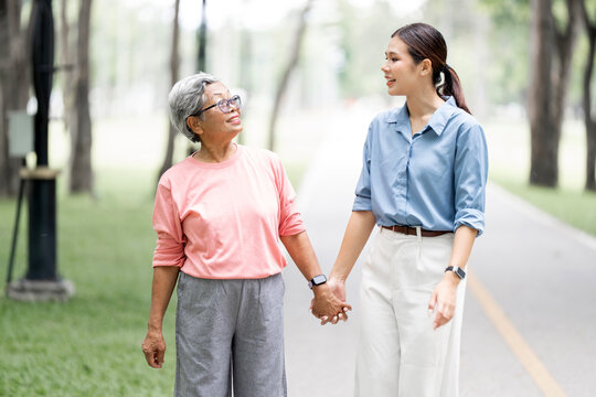 Smiling senior mother and adult daughter holding hands walking in park
