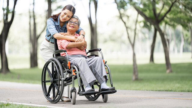 Happy Asian Daughter Hugging Senior Mother in Wheelchair at Park