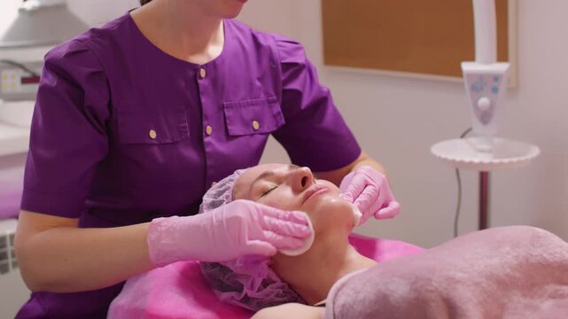 Facial toner. Detox procedure. Female beautician using cotton pads from client face removing moisturizing beauty mask in clinic.