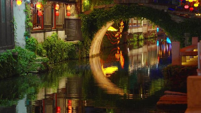 Lantern-lit canal and arched stone bridge reflected in water at night in Zhouzhuang