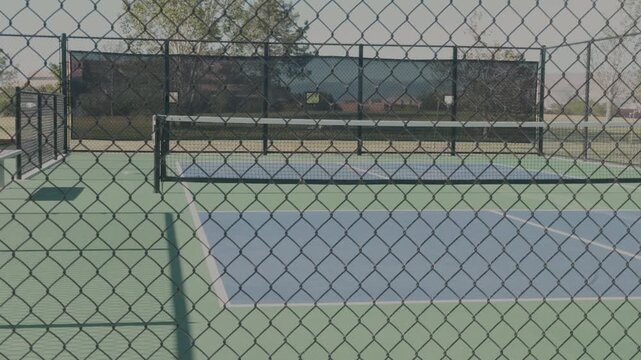 Still shot of outdoor pickleball courts seen through chain link fencing on a clear day.