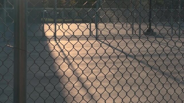 Still shot of empty pickleball court behind chain link fence in warm evening light.