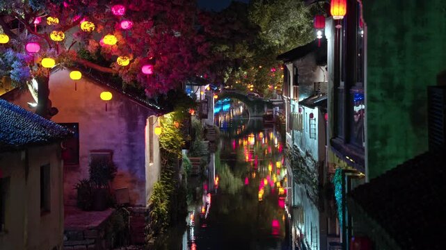 Vibrant lanterns hang over a tranquil canal in Zhouzhuang, casting colorful reflections on the water. Ideal for cultural documentaries or travel features.