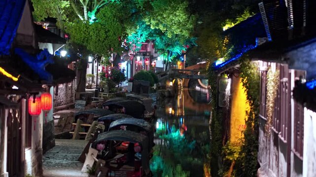 Gondolas line the illuminated canal in Zhouzhuang, with colorful lights reflecting on the water. Ideal for travel documentaries or cultural features.